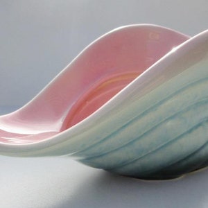 May include: A ceramic seashell planter with a pink interior and a blue and green exterior. The planter is glazed and has a smooth finish.