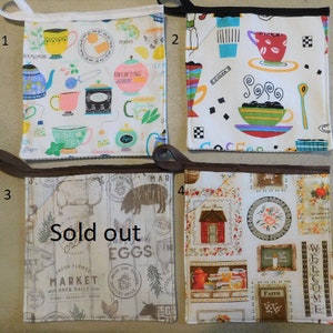 May include: Four different kitchen pot holders with various designs. The first pot holder has a white background with a teacup and teapot pattern. The second pot holder has a white background with a coffee cup and coffee pot pattern. The third pot holder has a white background with a farm animal and market pattern. The fourth pot holder has a white background with a farmhouse and floral pattern. The text "Sold out" is written on the third pot holder.