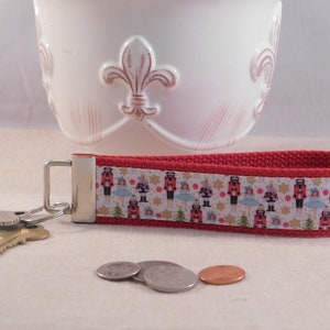 May include: Red key chain with a white ribbon featuring a repeating pattern of nutcracker figures. The ribbon is attached to a silver key ring.