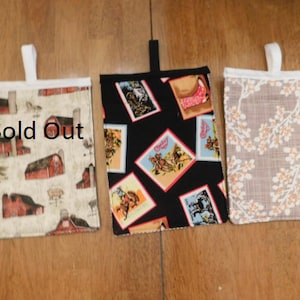 May include: Three fabric bags with white handles. The bag on the left has a red barn pattern. The middle bag has a black background with a colorful western pattern. The bag on the right has a beige background with a white floral pattern. The bag on the left says "Sold Out".