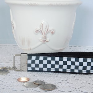 May include: Black and white checkered key chain with a silver key ring. The key chain is made of fabric and has a black border.