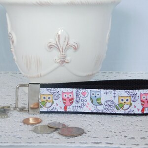 May include: A black and white key chain with a colorful owl pattern. The owls are pink, blue, yellow, and green. The key chain is made of fabric and has a metal ring.