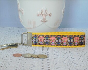 May include: A yellow key chain with a colorful skull pattern. The key chain has a silver metal ring and a silver metal clasp.