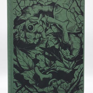 Può includere: Un raccoglitore per carte rettangolare di colore verde con un'illustrazione a linee nere di una creatura simile a un bruco tra foglie e motivi a crepe. La copertina riporta il testo CARD BINDER Collection nell'angolo in basso a destra.