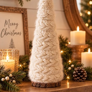 May include: A conical Christmas tree decoration made of cream-colored, chunky knit yarn with a fuzzy texture. The tree is mounted on a circular, natural brown wood slice base, showcasing a distinct braided stitch pattern throughout the exterior.