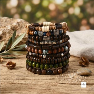 Pode incluir: Uma pilha de oito pulseiras de contas com várias contas de madeira castanho-escuras, verdes e claras, intercaladas com espaçadores de metal prateado, detalhes cilíndricos e berloques circulares com um design de árvore da vida.