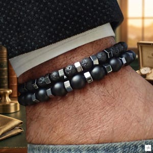 Puede incluir: Un conjunto de dos pulseras de cuentas con cuentas de piedra de lava negra porosa y cuentas de ónice negro mate liso, ambas acentuadas con pequeños espaciadores metálicos cúbicos de tono plateado pulido en un patrón alterno.
