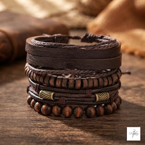 May include: A multi-layered bracelet set featuring dark brown leather straps, a row of cylindrical wooden beads, and a strand of round dark brown wooden beads. Two antique brass-toned metal accents are integrated into the leather cord section.