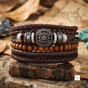 Puede incluir: Una pulsera de varias hebras con cordones de cuero trenzado marrón oscuro, una fila de cuentas de madera lisas y un dije metálico central con un patrón de estrella circular. El diseño incluye espaciadores cilíndricos plateados y oscuros.