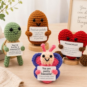 May include: Four crocheted figures including a green turtle, a brown potato, a pink and blue butterfly, and a red heart. Each figure holds a white card with printed text messages including Positive potato, You're Turtle-y Awesome, and Pocket Heart.