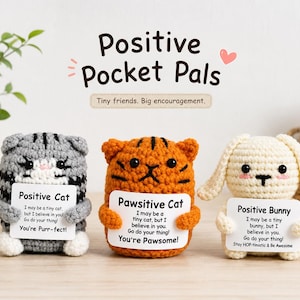 May include: Three crocheted figures labeled Positive Pocket Pals: a gray tabby cat, an orange tiger cat, and a cream-colored bunny. Each figure holds a white card with printed text offering encouragement. The text includes phrases like You're Purr-fect, You're Pawsome, and Stay HOP-timistic & Be Awesome.