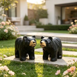 May include: Two carved wooden bear figurines standing side by side. Each bear features a textured black body with a smooth, light-coloured tan face and snout. The figures have visible chisel marks across their surfaces, creating a faceted appearance.