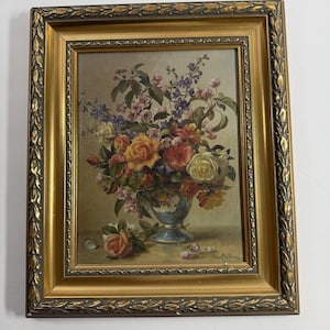 May include: A framed oil painting depicting a vibrant floral arrangement in a blue and white vase. The bouquet features yellow, red, and white roses with purple accents. The frame is ornate gold with dark detailing. The artist signature reads Albert Williams.