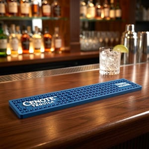 Puede incluir: Una alfombrilla de bar rectangular de goma azul con una superficie texturizada de pequeños círculos en relieve. La alfombrilla presenta el texto impreso en blanco "CENOTE TEQUILA" a la izquierda y "TEQUILA with a SOUL" a la derecha, diseñada para recoger derrames.