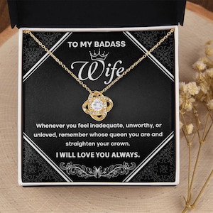 May include: A gold-tone necklace with a central knot pendant featuring a clear crystal, presented in a black gift box. The box insert displays the text: TO MY BADASS Wife, Whenever you feel inadequate, unworthy, or unloved, remember whose queen you are and straighten your crown. I WILL LOVE YOU ALWAYS.