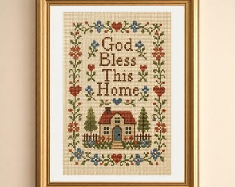 May include: A framed cross-stitch sampler on beige fabric featuring the text God Bless This Home in brown letters. The design includes a central house with a red roof, green trees, and a decorative border of red hearts and blue and orange flowers.