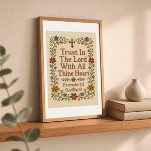 May include: A framed cross-stitch embroidery featuring the text Trust In The Lord With All Thine Heart Proverbs 3:5 in dark red lettering, surrounded by a decorative floral border with blue, red, and yellow flowers and a small cross at the top.