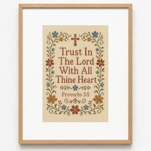 May include: A framed cross-stitch embroidery on beige fabric featuring the text "Trust In The Lord With All Thine Heart" and "Proverbs 3:5" in red. The design is surrounded by a floral border with blue, red, and yellow flowers and green vines.