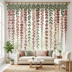Op de afbeelding: Een decoratieve raamhanger met meerdere verticale strengen van gehaakte blauweregenbloemen in roze en crèmetinten, afgewisseld met groene gehaakte bladranken, allemaal opgehangen aan een horizontale houten roede aan de bovenzijde.
