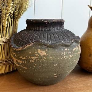 May include: A round ceramic vessel with a wide opening, featuring a dark brown, ribbed upper section and a distressed, sage green lower body. The rim has a wavy, scalloped edge that separates the two distinct color zones of the pot.