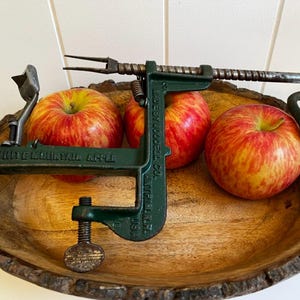 Peut inclure: Un éplucheur de pommes White Mountain en fonte vert foncé avec une manivelle en métal, une fourchette à trois dents et une base à vis. L'outil présente un texte en relief indiquant White Mountain Apple et Made by Goodell Co. Antrim N.H. USA.