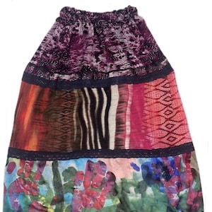 May include: A knee-length skirt featuring an elastic waistband and three horizontal panels separated by black lace trim. The top panel is purple with a dark animal print, the middle panel has varied patterns, and the bottom panel displays handprints.