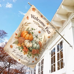 May include: A rectangular garden flag featuring the text Welcome Fall and The Smiths Family. The design displays a cluster of orange, white, and green pumpkins, autumn leaves, wheat stalks, and flowers on a cream-colored background.