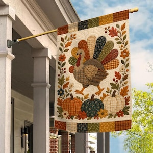 May include: A rectangular fabric garden flag featuring a central turkey with a multi-colored patterned tail, surrounded by autumn leaves, flowers, and three pumpkins in orange, dark green, and white, all set against a cream-colored background.