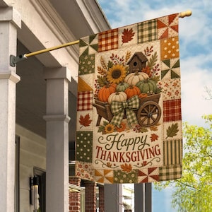 May include: A rectangular garden flag featuring a patchwork quilt design with autumn colors and patterns. The center displays a wooden cart filled with pumpkins, sunflowers, and a birdhouse, accented by a plaid bow. The text reads Happy Thanksgiving.