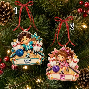 May include: Two bowling-themed Christmas ornaments hanging by red ribbons. Ornament 1 features a boy in a blue shirt with the name ADAM and 2026. Ornament 2 features a girl in a pink outfit with the name LUGI and 2026. Both show characters bowling.