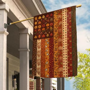 May include: A rectangular garden flag featuring a vertical striped pattern with autumn-themed motifs including fall leaves, acorns, mushrooms, small birds, ladybugs, and floral elements in shades of orange, brown, red, yellow, and dark green.