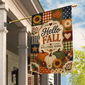 May include: A rectangular garden flag featuring a patchwork design with sunflowers, pumpkins, and autumn leaves. The center displays the text Hello FALL WELCOME HOME in a decorative frame. The flag is mounted on a gold metal pole attached to a white porch pillar.