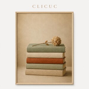 Puede incluir: Una lámina enmarcada con una pila de cinco libros en tonos apagados de verde salvia, beige y terracota. Una flor de hortensia seca descansa sobre el libro superior. El texto CLICUC está impreso en color marrón claro en la parte superior central.