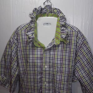 May include: A short-sleeved button-down shirt featuring a plaid pattern in shades of purple, lime green, and white. The shirt includes a distinctive ruffled collar detail with a lime green and white plaid interior lining and a front button closure.