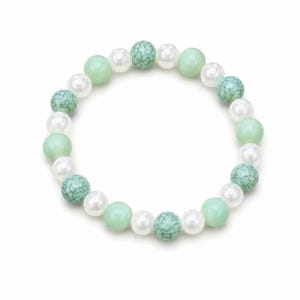Puede incluir: Una pulsera de cuentas con un patrón repetitivo de perlas blancas redondas, cuentas de color verde claro lisas y cuentas de color turquesa con una textura agrietada oscura. La disposición circular alterna estos tipos de cuentas.