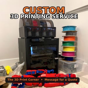 May include: A black Bambu Lab 3D printer with an AMS unit on top, featuring text that reads CUSTOM 3D PRINTING SERVICE. A stack of colourful filament spools sits to the right, and a red and blue articulated 3D printed figure lies in the foreground.