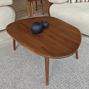 May include: A brown wooden coffee table with an organic, rounded shape and four tapered legs. Two small, dark, textured spherical objects are placed on the smooth, polished surface of the table, which features visible wood grain patterns.