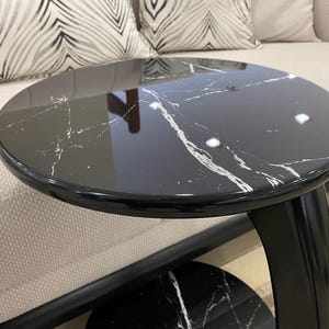 May include: A round side table featuring a glossy black surface with white marble veining. The table has a curved black support structure and a matching circular base, providing a sleek and reflective finish for this functional furniture piece.