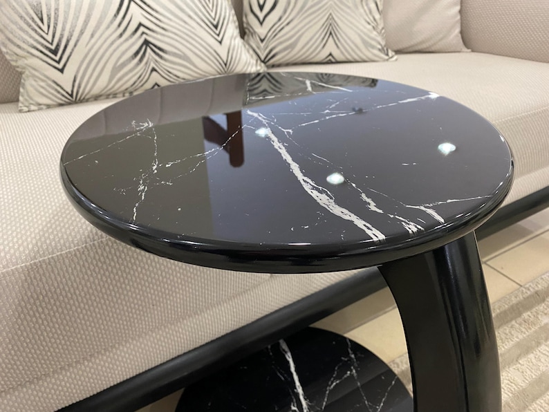 May include: A round side table featuring a glossy black surface with white marble veining. The table has a curved black support structure and a matching circular base, providing a sleek and reflective finish for this functional furniture piece.
