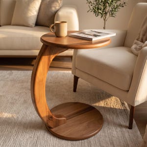 May include: A C-shaped side table crafted from warm-toned wood, featuring a circular base and a matching circular tabletop. The table has a smooth, polished finish that highlights the natural grain of the wood, providing a stable surface.