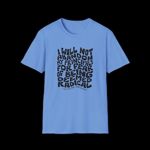 May include: A light blue short-sleeved t-shirt featuring black text that reads: I WILL NOT ABANDON MY PRINCIPALS FOR FEAR OF BEING DEEMED RADICAL, followed by the name ZOHRAN MAMDANI in a wavy, distorted font style across the centre chest area.