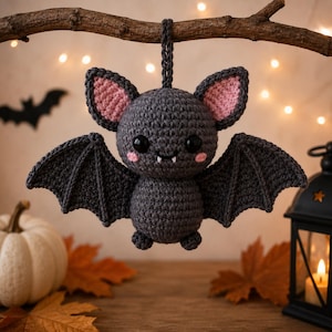 Può includere: Un pipistrello decorativo realizzato all'uncinetto in grigio scuro con grandi occhi neri, interno delle orecchie rosa e due piccole zanne bianche. Il peluche presenta un corpo arrotondato, ali appuntite e un occhiello per appenderlo.