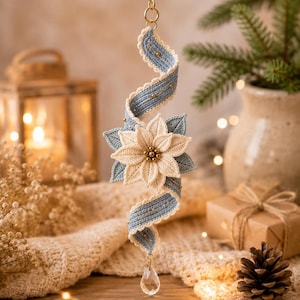 May include: A hanging ornament featuring a central cream-colored crocheted poinsettia flower with a gold bead center, surrounded by light blue crocheted leaves and a spiraling blue ribbon accented with gold beads, finished with a clear crystal drop.