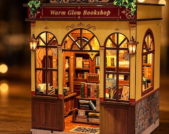 Puede incluir: Una maqueta de librería de madera titulada Warm Glow Bookshop, con ventanas arqueadas, dos faroles exteriores y un interior lleno de estanterías detalladas con libros, un pequeño globo terráqueo e iluminación cálida.