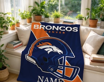 Könnte beinhalten: Eine marineblaue und orangefarbene Fleecedecke mit dem Denver Broncos Logo, einer Footballhelm-Grafik und dem Text BRONCOS DENVER NAME. Das Design zeigt eine große Helm-Illustration, die mittig auf dem Stoff platziert ist.