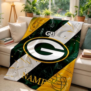 May include: A plush throw blanket featuring a Green Bay Packers theme with a large central G logo, football helmet graphics, and the text GB and NAME. The design uses diagonal stripes of dark green, gold, and white with star accents.