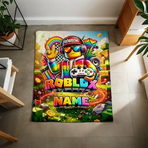 May include: A rectangular blanket featuring a colorful graphic of a Roblox character wearing headphones and sunglasses, holding a game controller. The design includes a rainbow, gold coins, and the text ROBLOX and NAME in bold, multi-colored letters.