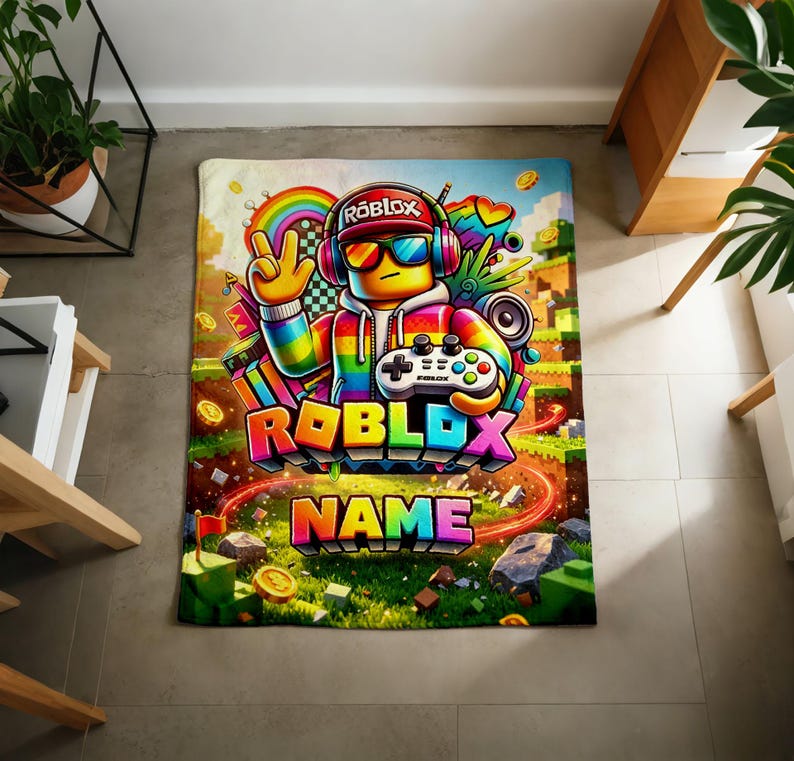 May include: A rectangular blanket featuring a colorful graphic of a Roblox character wearing headphones and sunglasses, holding a game controller. The design includes a rainbow, gold coins, and the text ROBLOX and NAME in bold, multi-colored letters.
