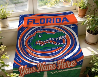 Könnte beinhalten: Eine rechteckige Fleecedecke mit blau-orangem Design, dem Wort FLORIDA in blauer Schrift, einer grünen Alligatorgrafik und dem Text Your Name Here in oranger Schreibschrift, vor einem Hintergrund aus konzentrischen Kreisen und Sternen.