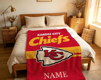 Könnte beinhalten: Eine rote Fleecedecke mit dem Kansas City Chiefs Logo und Schriftzug in Gelb und Weiß. Das Design zeigt den Schriftzug Kansas City Chiefs oben, das pfeilspitzenförmige Teamlogo in der Mitte und das Wort NAME im unteren Bereich.